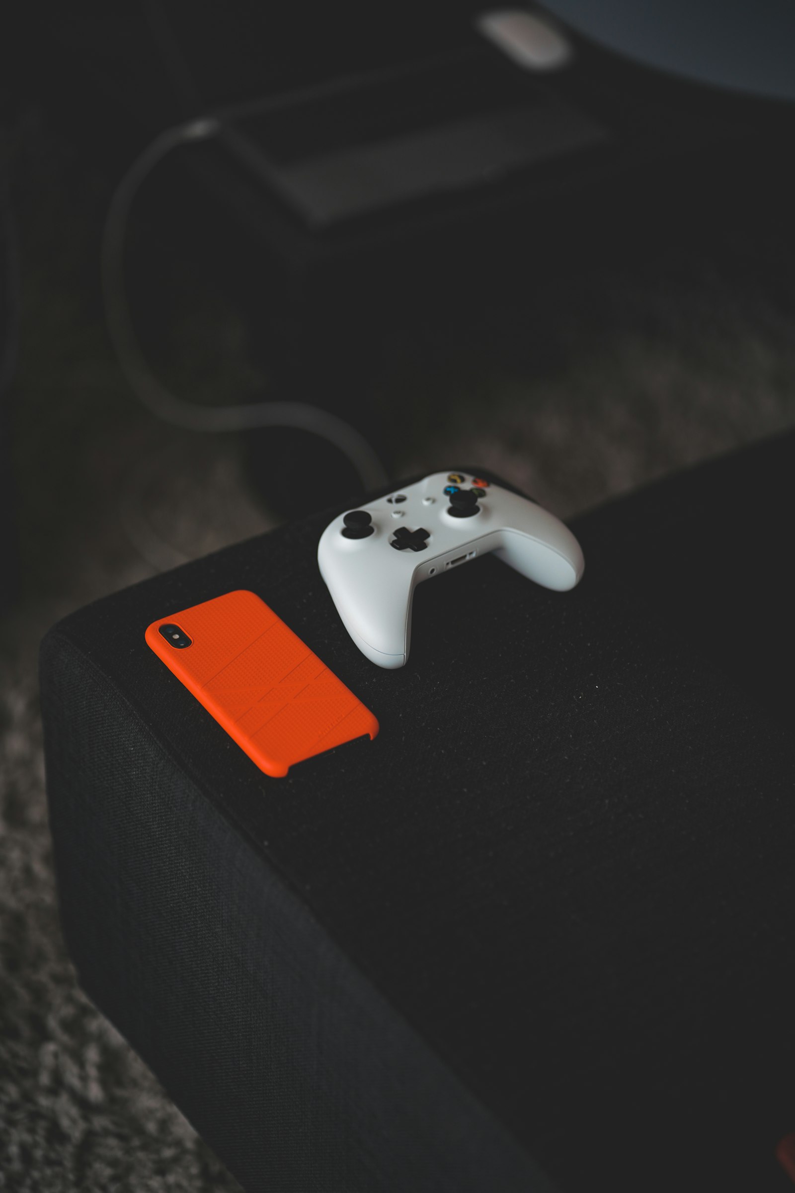A white game controller and an orange phone on the arm of a couch, ready for a quick walkthrough check
