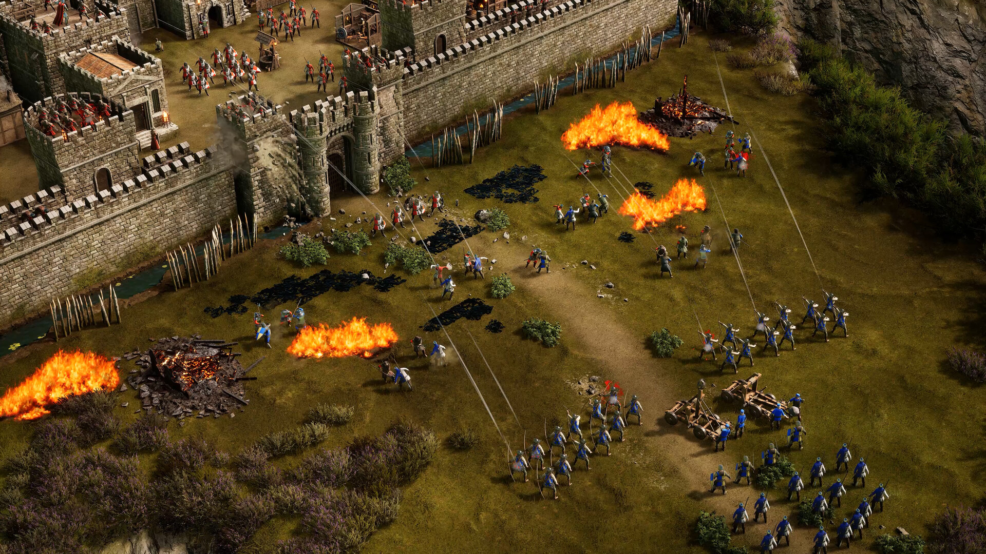 Stronghold 4 screenshot: an army attacking castle walls, with fires burning in the field
