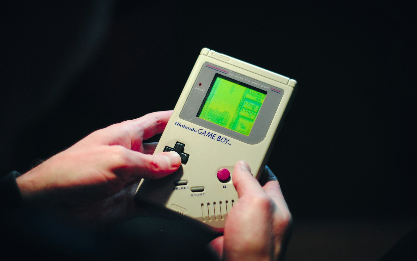 Hands holding an original Game Boy, a classic handheld many players still replay