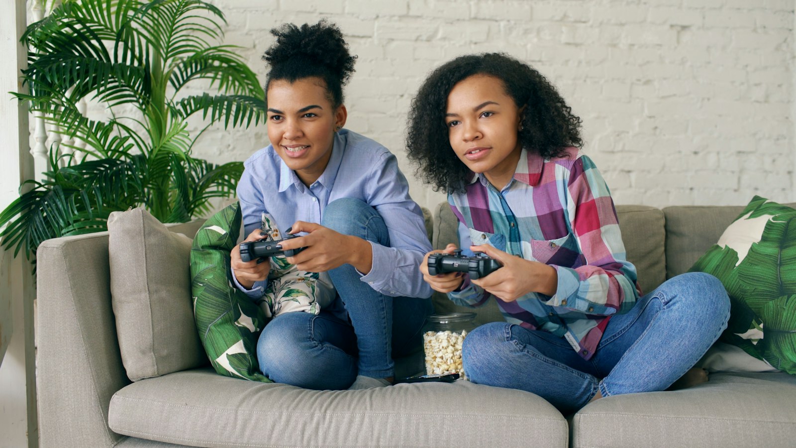 Two friends playing a console game side by side on a couch